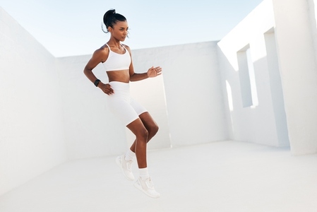 Full length of a slim female in white sportswear jumping outdoors  Professional fitness athlete doing warming up exercises