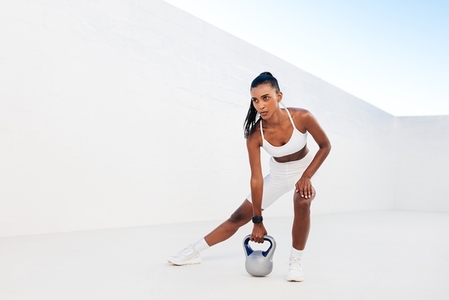 Full length of slim woman exercising with kettlebell outdoors  Professional fitness athlete doing intense training with weights in a white outdoor studio