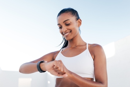 Smiling female in a white fitness bra looking at a smartwatch and checking her heart rate