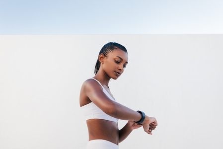 Side view of slim female in white sports bra looking on a smartwatch  Young sportswoman checking heart rate