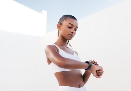 Confident female athlete checking her pulse  Healthy woman in a white sports bra looking on smartwatch