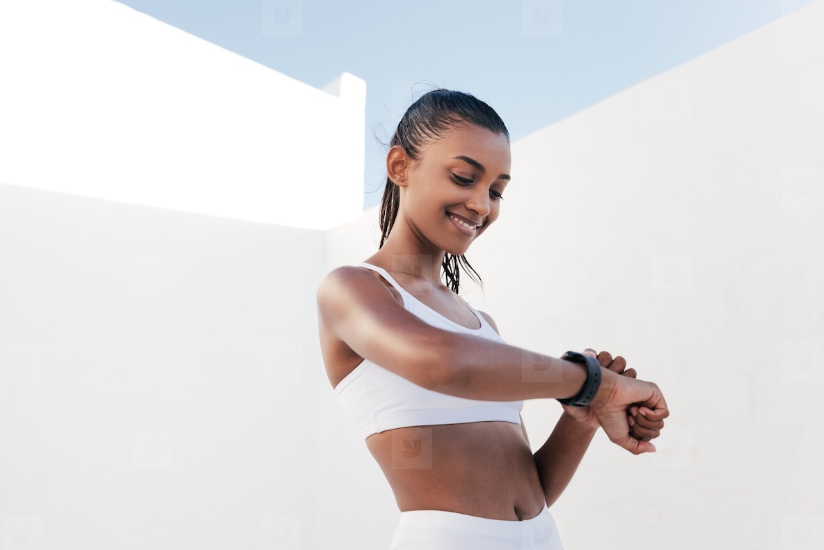 Smiling fitness influencer with a smartwatch. Slim healthy woman checking her heart rate outdoors