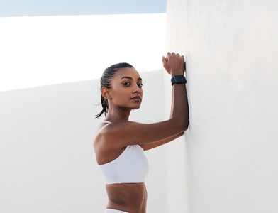 Confident slim female relaxing at the wall  Young fitness influencer in sports bra looking at camera