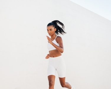 Confident woman sprinting against a white wall  Slim jogger in white fitness attire running outdoors