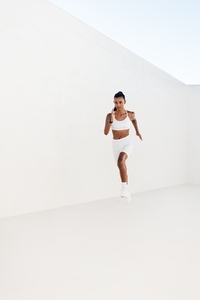 Full length of a slim female sprinting against a white wall  Young athlete jogging outdoors
