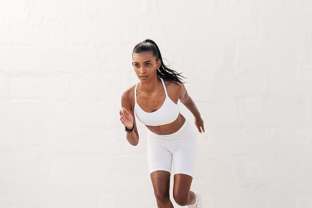 Young slim female athlete running outdoors against a white wall. Fitness influencer in white sportswear sprinting