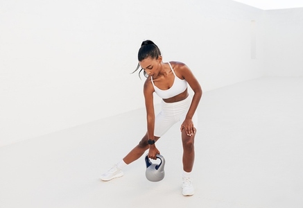 Slim female in a white sports bra doing intense training with a kettlebell  Full length of a fitness influencer outdoors