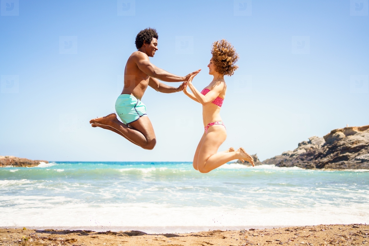 Happy diverse couple jumping near sea