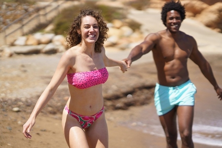 Happy multiracial couple holding hands while having fun near sea