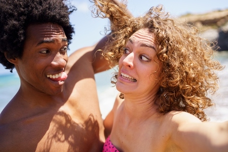 Selfie of funny diverse couple making faces on beach
