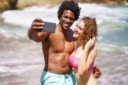 Smiling diverse couple taking selfie near sea