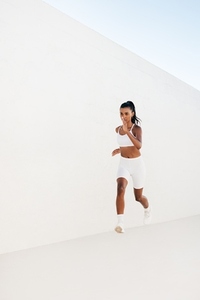 Full length of a slim female sprinting outdoors  Woman jogging outdoors at white wall