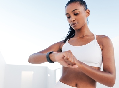 Slim female athlete looking at smartwatch  Woman in white fitness clothes standing outdoors checking her heart rate