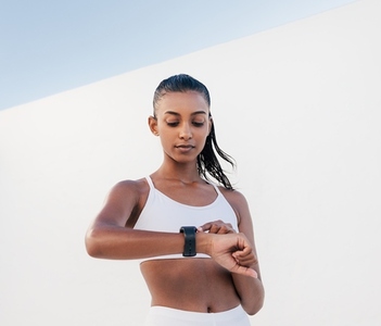 Portrait of a young female checking her pulse  Woman in a fitness bra adjusting her smartwatch