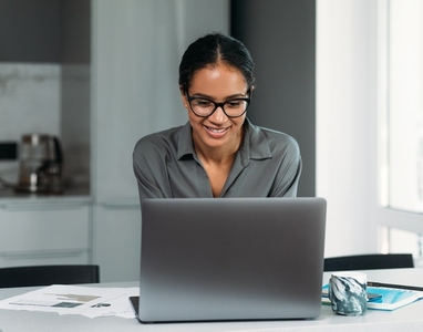 Smiling female in eyeglasses working on a laptop at the kitchen counter