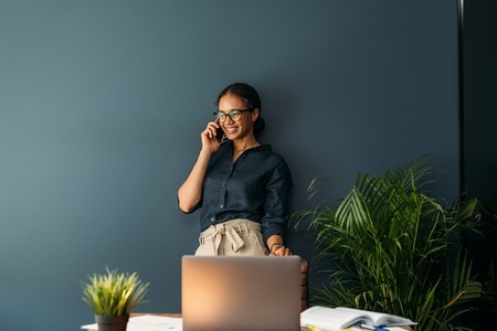 Cheerful businesswoman in formal wear leaning blue wall in home office