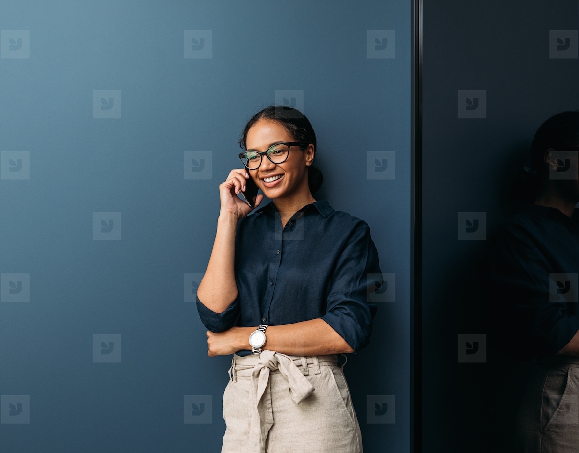 Smiling woman in formal clothes leaning blue wall talking on a mobile phone