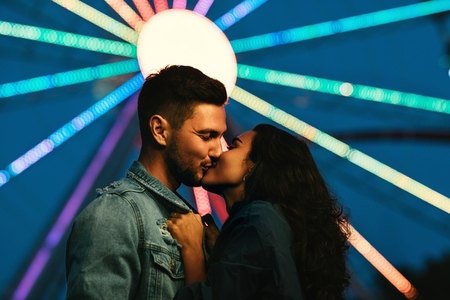 Young couple kissing in front of a Ferris wheel  Girl kissing her boyfriend in an amusement park at night