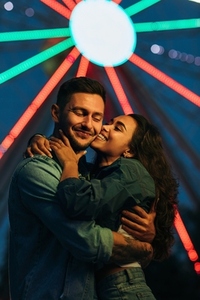 Young happy couple against Ferris wheel during the festival  Woman kissing her smiling boyfriend at night
