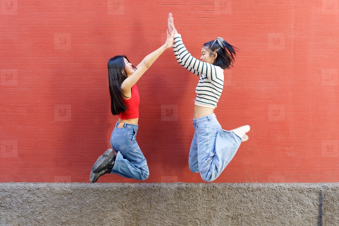 Joyful young Asian women giving high five while jumping