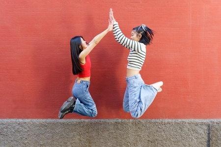Joyful young Asian women giving high five while jumping