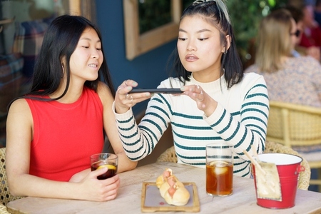 Delighted Asian female friends taking photo of food in cafe
