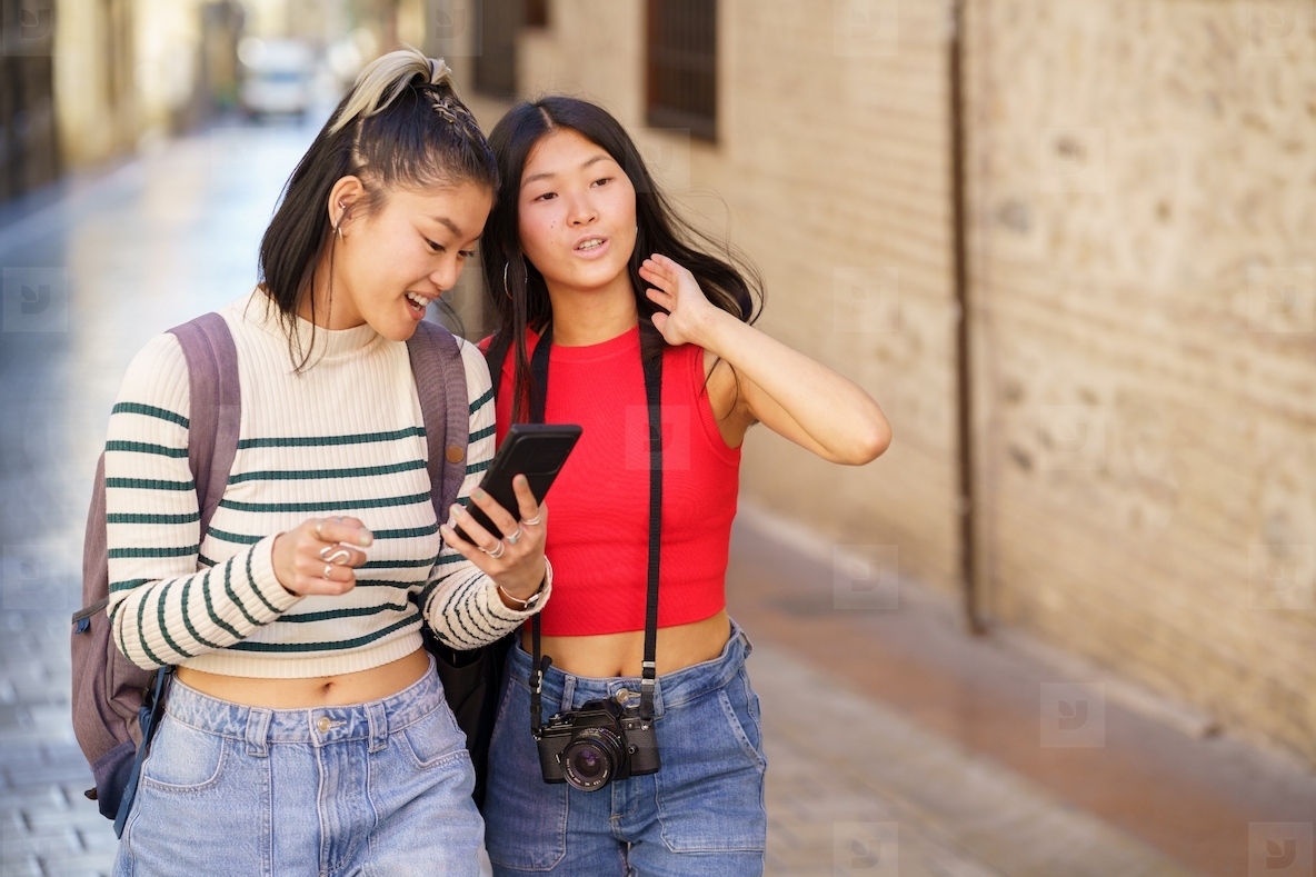Asian girls tourists walking on city street with smartphone