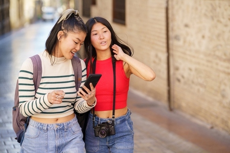 Asian girls tourists walking on city street with smartphone