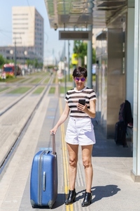 Positive woman with suitcase browsing smartphone on street