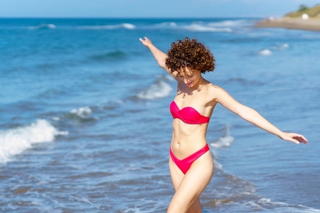 Joyful young lady in swimwear walking in sea with outstretched arms