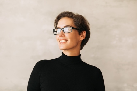 Portrait of a smiling businesswoman with short hair  Positive female in eyeglasses wearing black formal wear and looking away