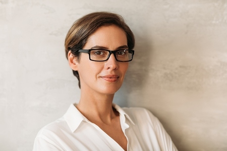 Portrait of a beautiful woman in eyeglasses leaning against a wall and looking at camera  Business female with short hair looking at the camera