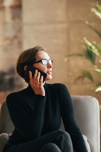 Businesswoman in eyeglasses wearing black formal clothes talking on mobile phone