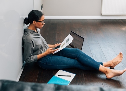 Full length of female entrepreneur sitting at home holding documents