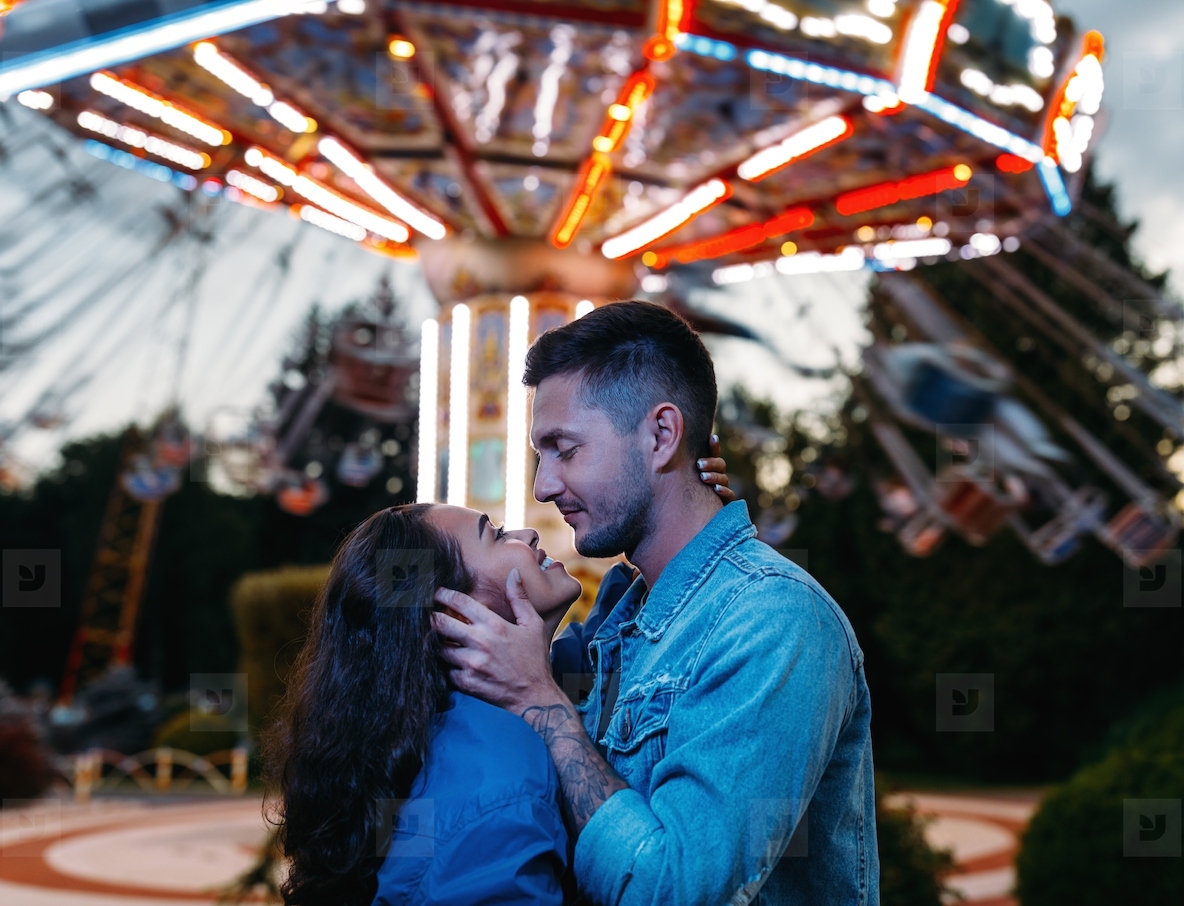 Happy couple in an amusement park. Young couple in love hugging and looking at each other against the carousel