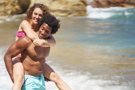 Black man carrying girlfriend near sea