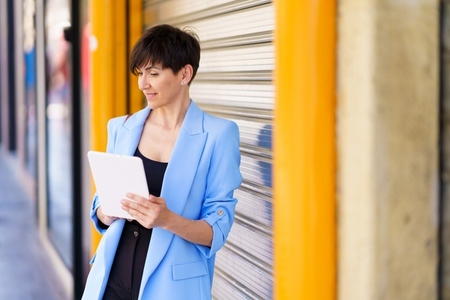 Serious woman with tablet standing against door in city