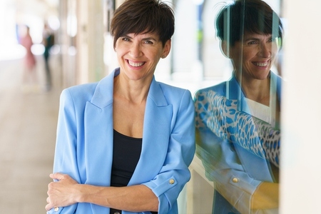 Cheerful mature woman leaning on glass wall and smiling
