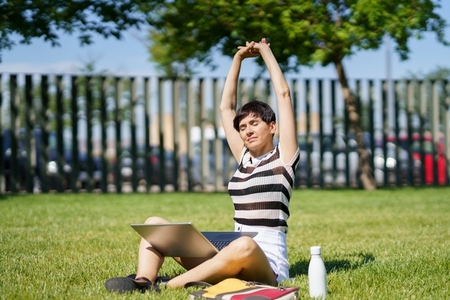 Content woman with laptop stretching arms in park