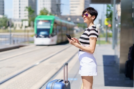 Young woman with suitcase using smartphone in train station