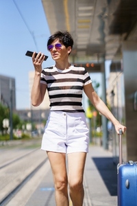 Young woman with suitcase and smartphone on street