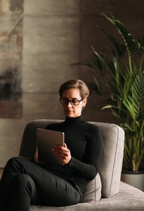 Businesswoman in black formal wear using digital tablet while sitting in her loft