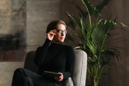 Middle aged businesswoman adjusting her eyeglasses and looking away