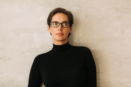 Portrait of a confident businesswoman in black formal wear looking at the camera while standing at the wall