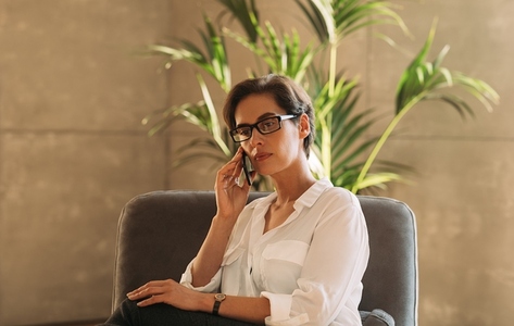 Middle aged businesswoman in formal wear talking on mobile phone while sitting indoors