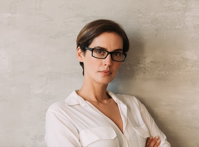 Portrait of a middle aged businesswoman in eyeglasses leaning on a wall looking straight at a camera