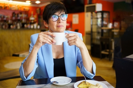Pensive mature woman drinking coffee in cafe