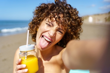 Happy woman taking selfie with drink on beach