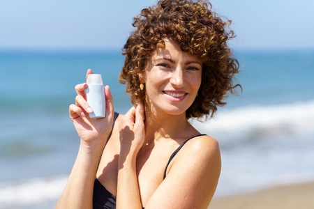 Smiling woman showing white tube of cosmetic product on beach