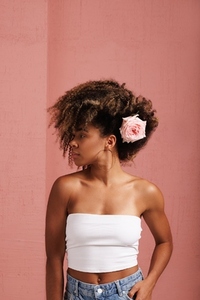 Young woman with a lush hairstyle with flower looking away standing at a pink wall
